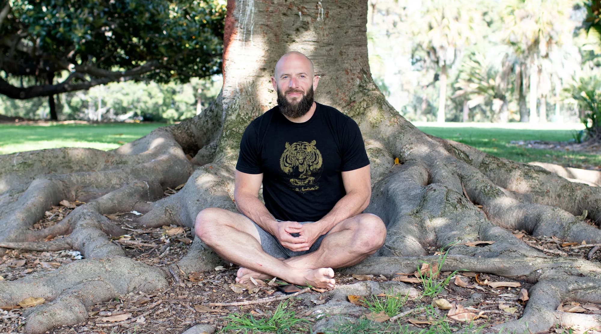 Miles sitting cross-legged among the roots of a banyan tree